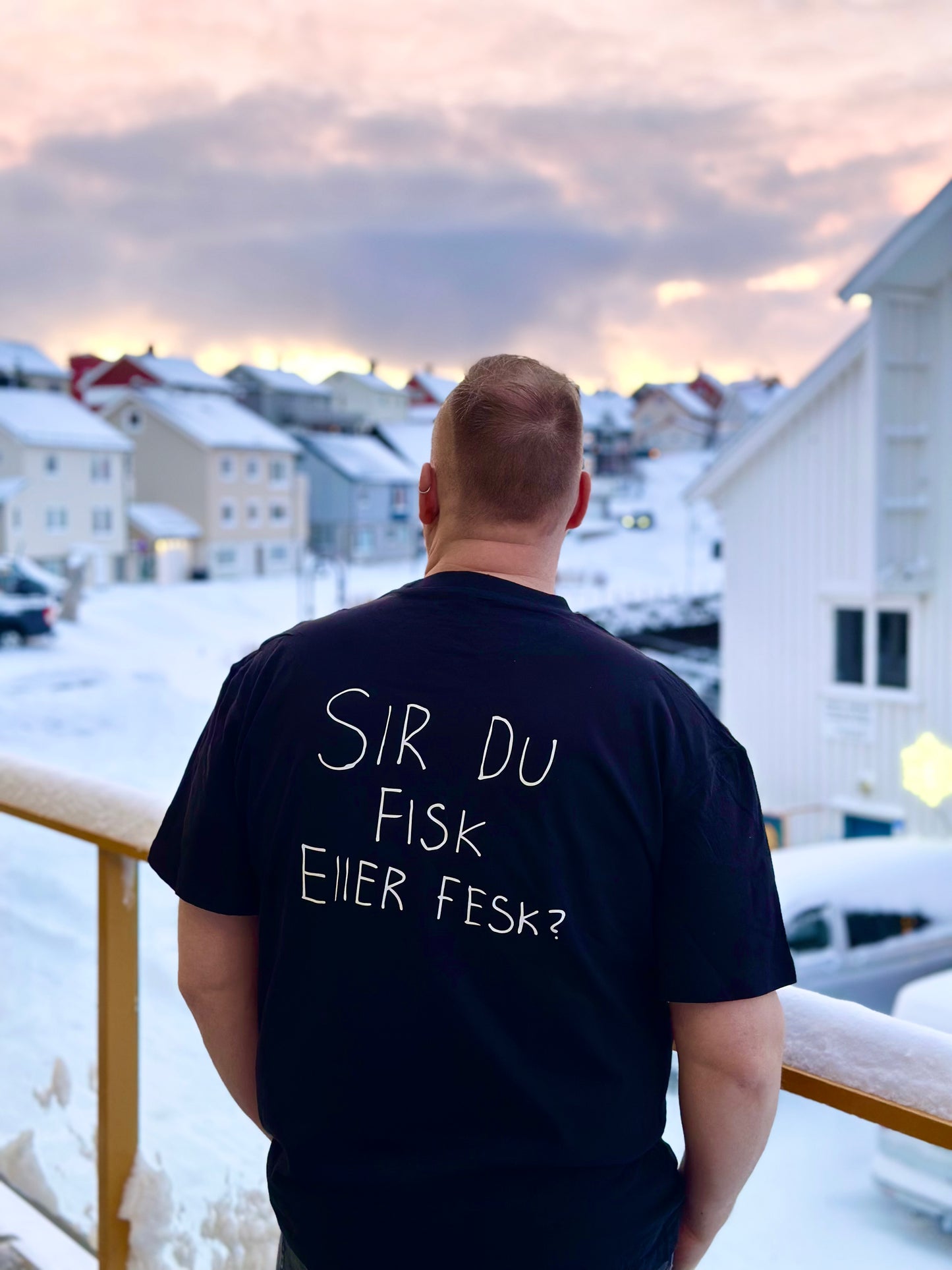Mann bakfra i svart t-skjorte med teksten Sir du fisk eller fesk? på ryggen