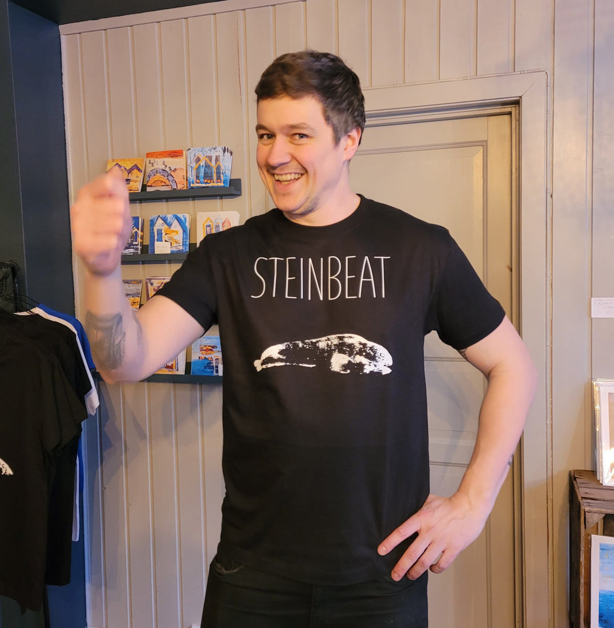 Mann i svart t-skjorte med teksten STEINBEAT og hvitt fisketrykk