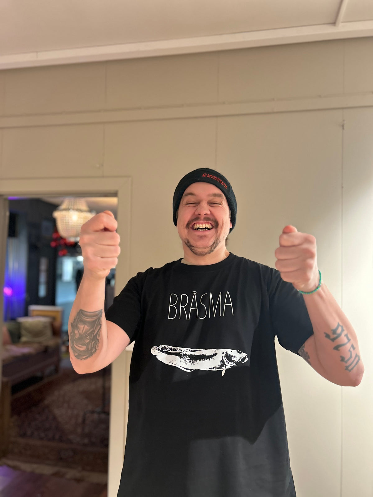 Mann i svart t-skjorte med teksten BRÅSMA og hvitt fisketrykk