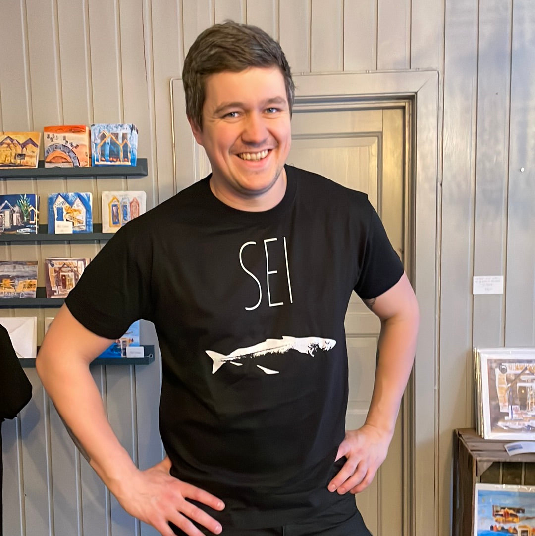 Mann i svart t-skjorte med teksten SEI og hvitt fisketrykk