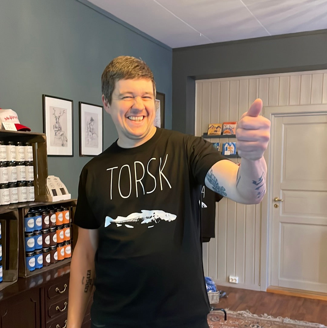 Mann i svart t-skjorte med teksten TORSK og hvitt fisketrykk