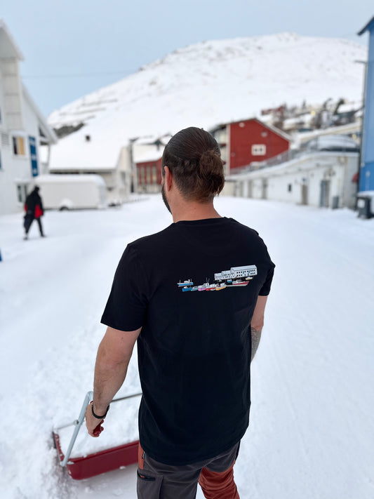 Svart t-skjorte med trykk på ryggen, fotografert bakfra i snøen i Honningsvåg