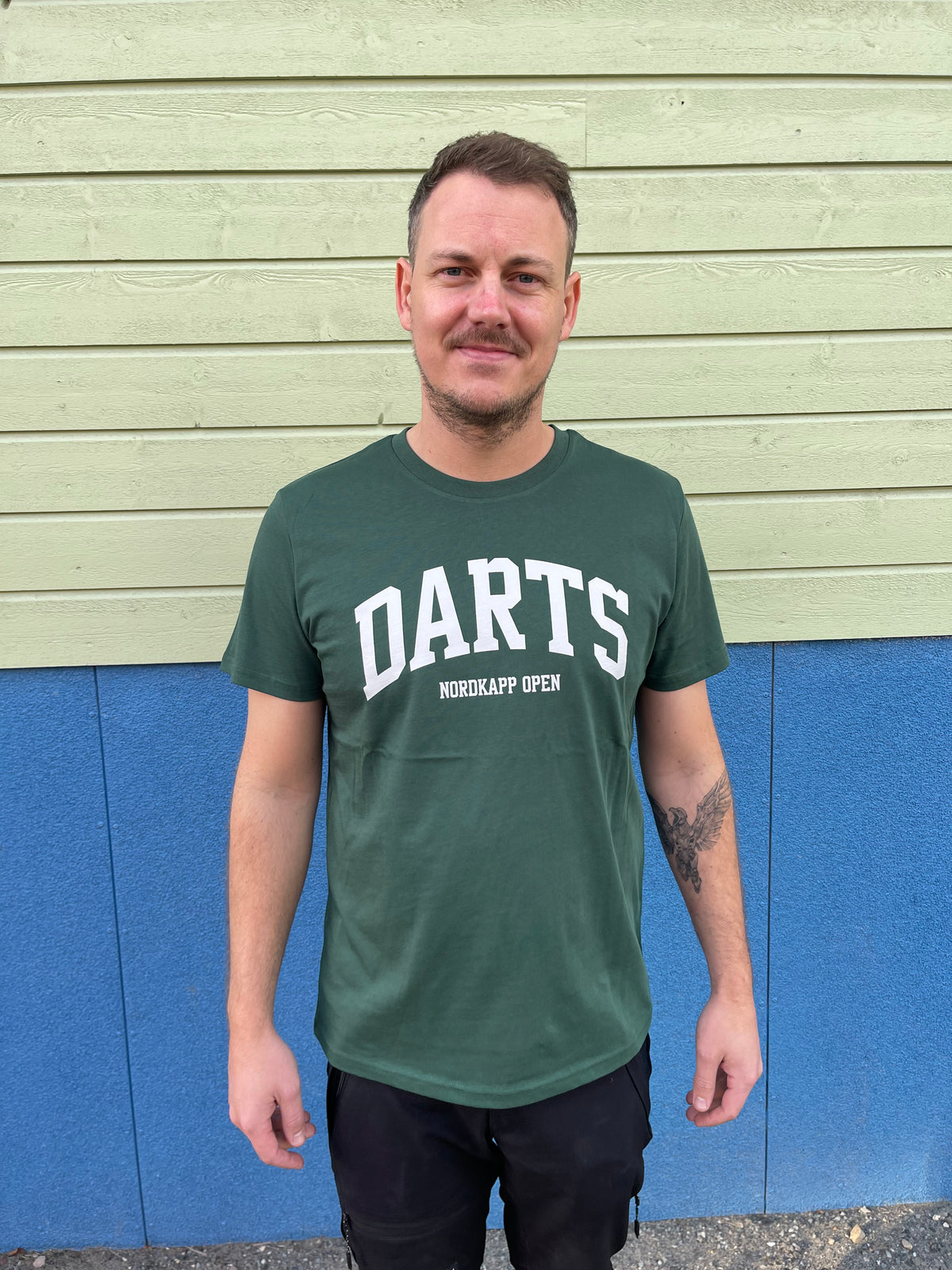 Mann i grønn t-skjorte med DARTS og NORDKAPP OPEN i hvitt
